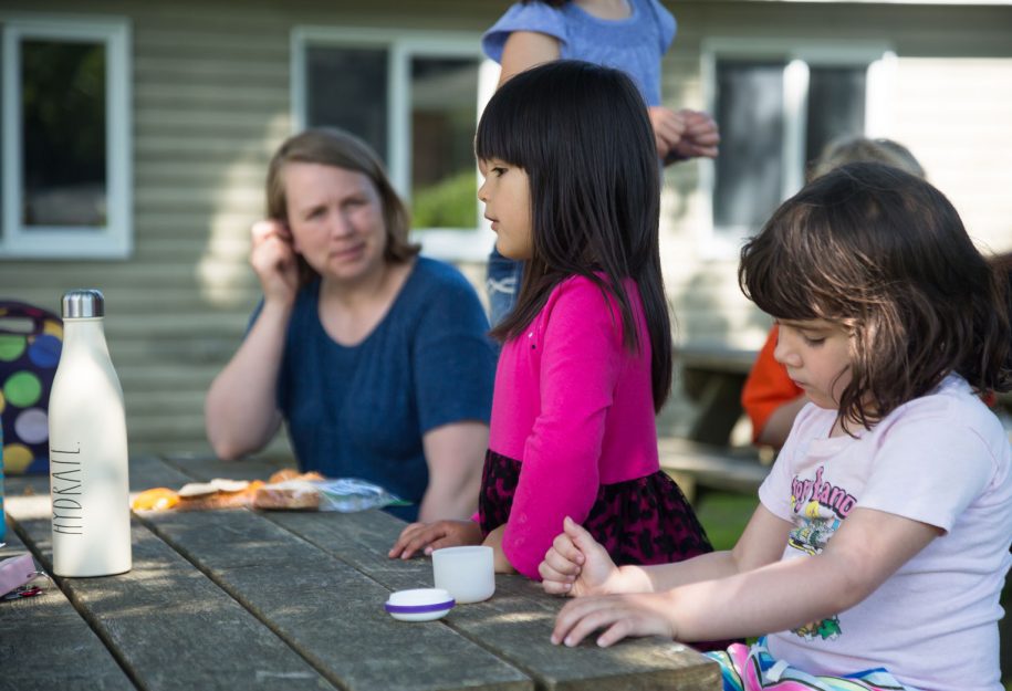 A young girl at summer camp sitting at a picnic table.